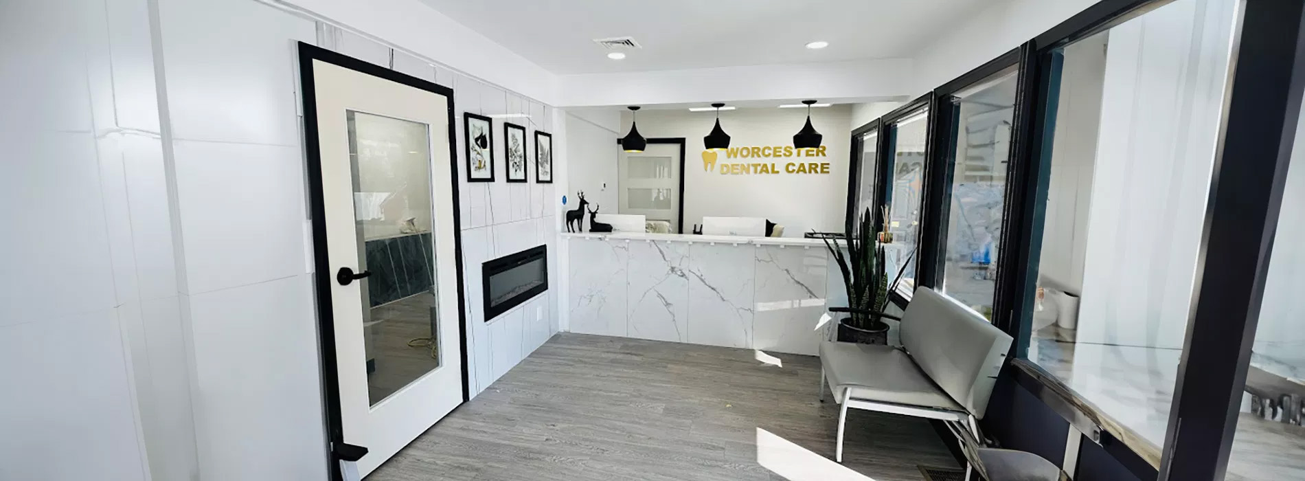 The image depicts an interior space, likely a modern waiting area or office reception area, with a clean and minimalist design, featuring a white tiled floor, a black door, and a white wall with framed artwork.