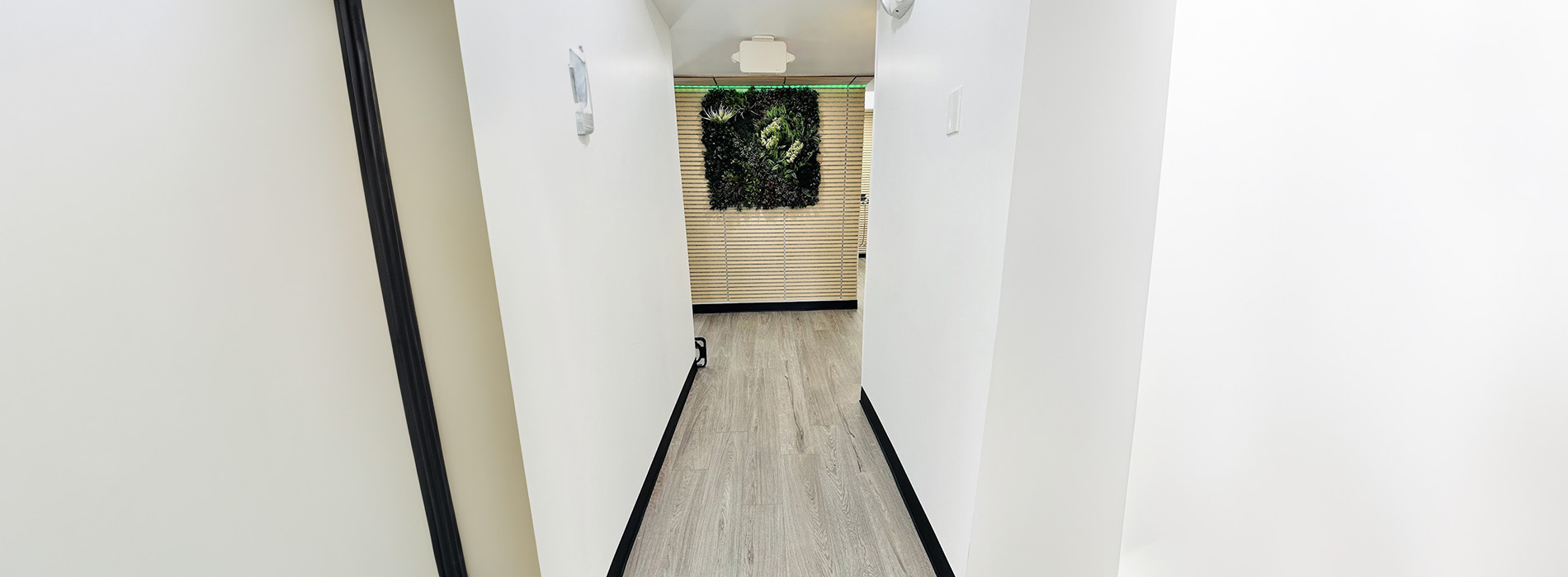The image shows a hallway with a black railing leading to a room with a white door on the right side.